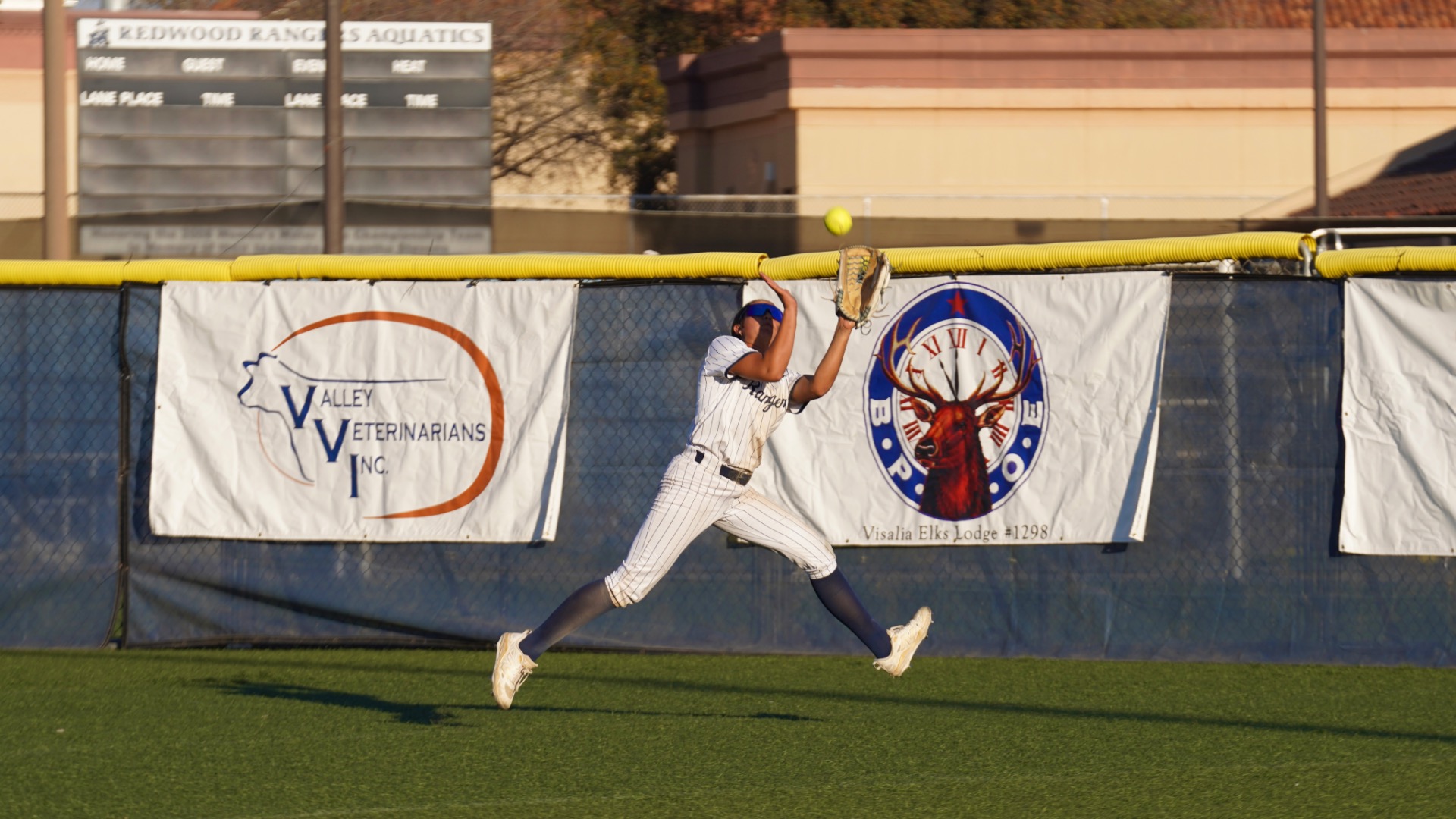 Slide 0 - Outfielder Rayah Rodriguez #11 leaping to catch a fly ball at the fence.
