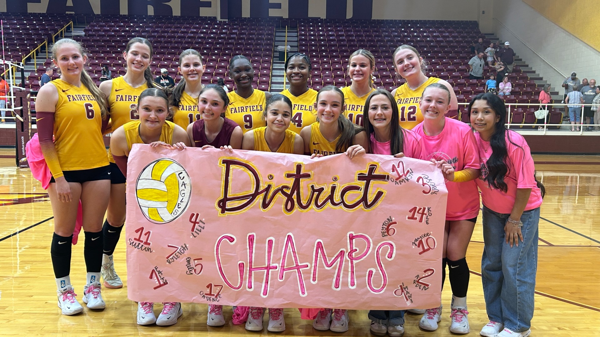 Girls on a volleyball court wearing gold uniforms.