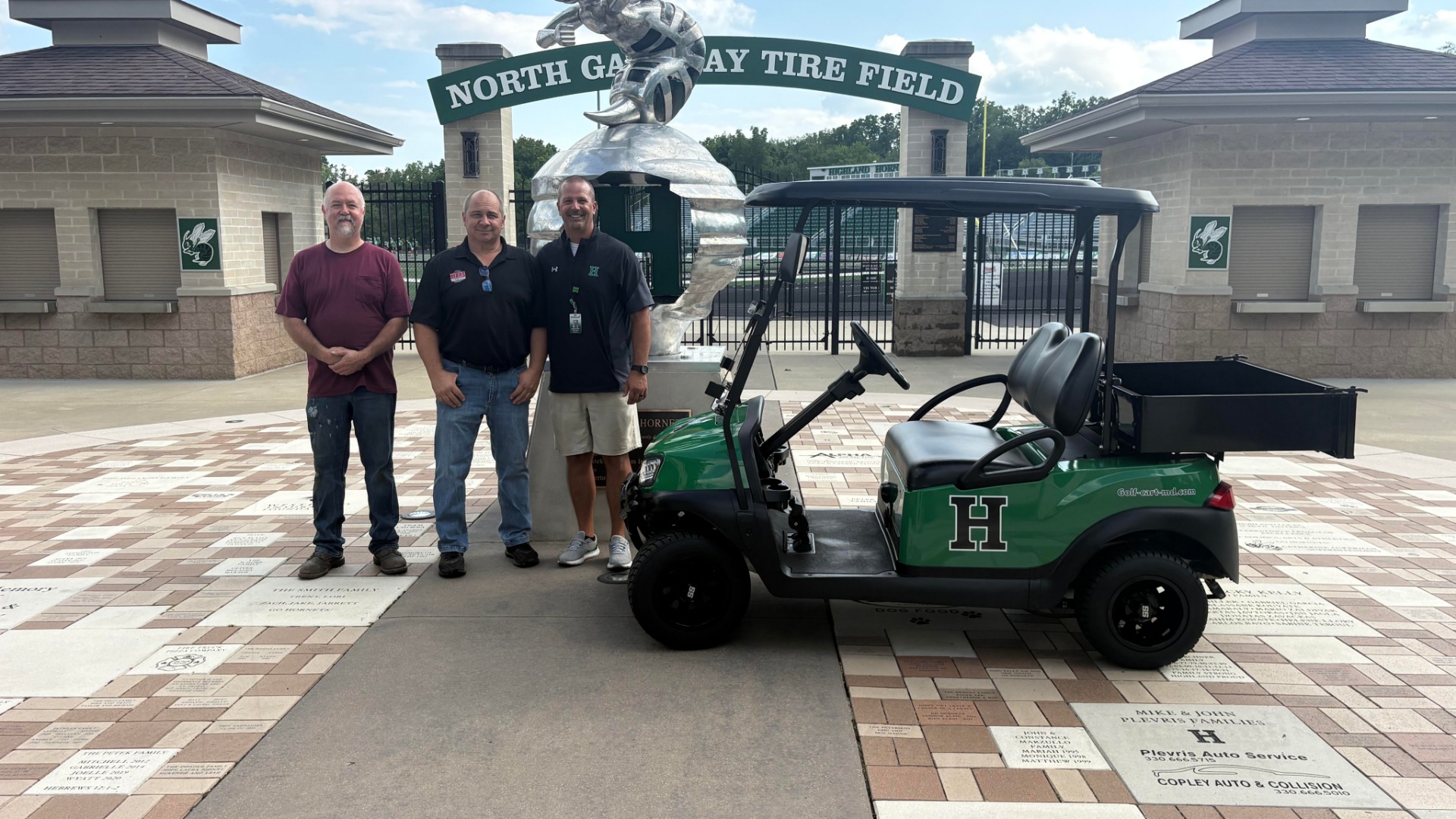 A picture of three people with a donated golf cart to the highland athletic dept.
