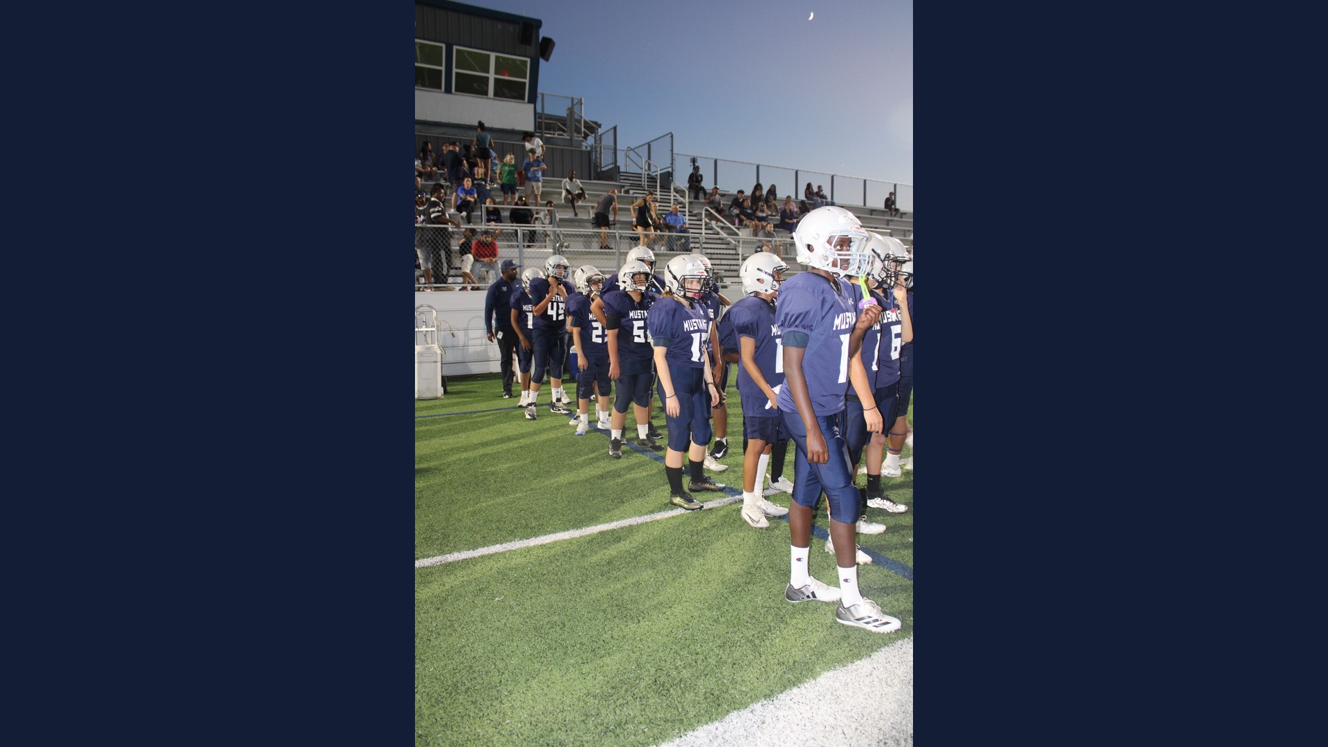 Lamar Mustangs football players in navy uniforms and silver helmets line up along the sideline.